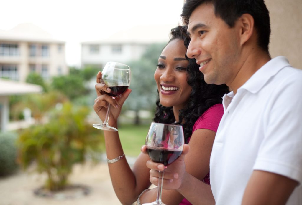 Man and woman enjoying wine over their balcony at the Grand Caymanian Resort.