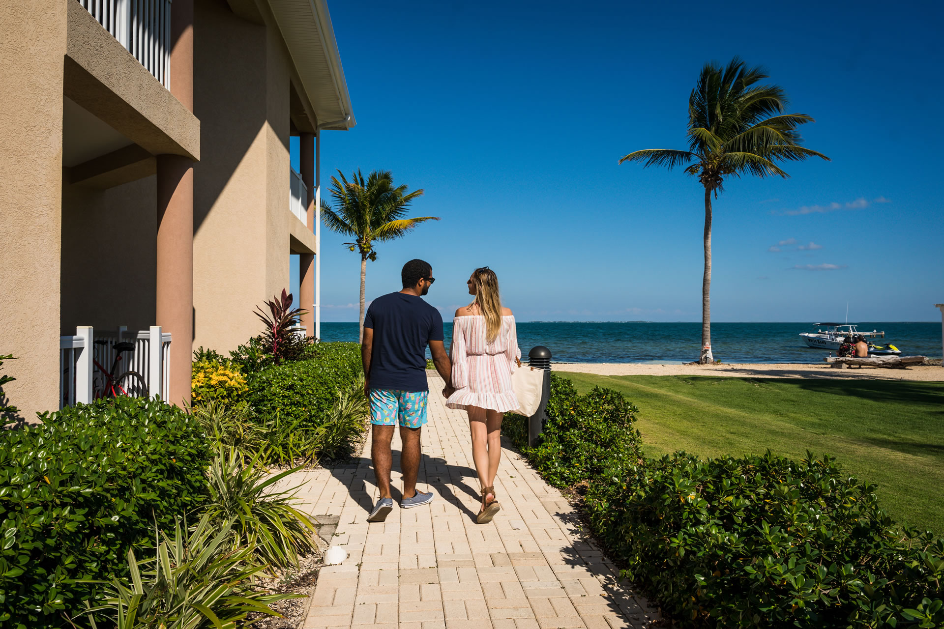 A couple walking down a pathway towards the beach at the Grand Caymanian Resort.