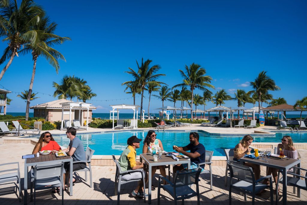 Several groups of people dining near the pool at the Grand Caymanian Resort.