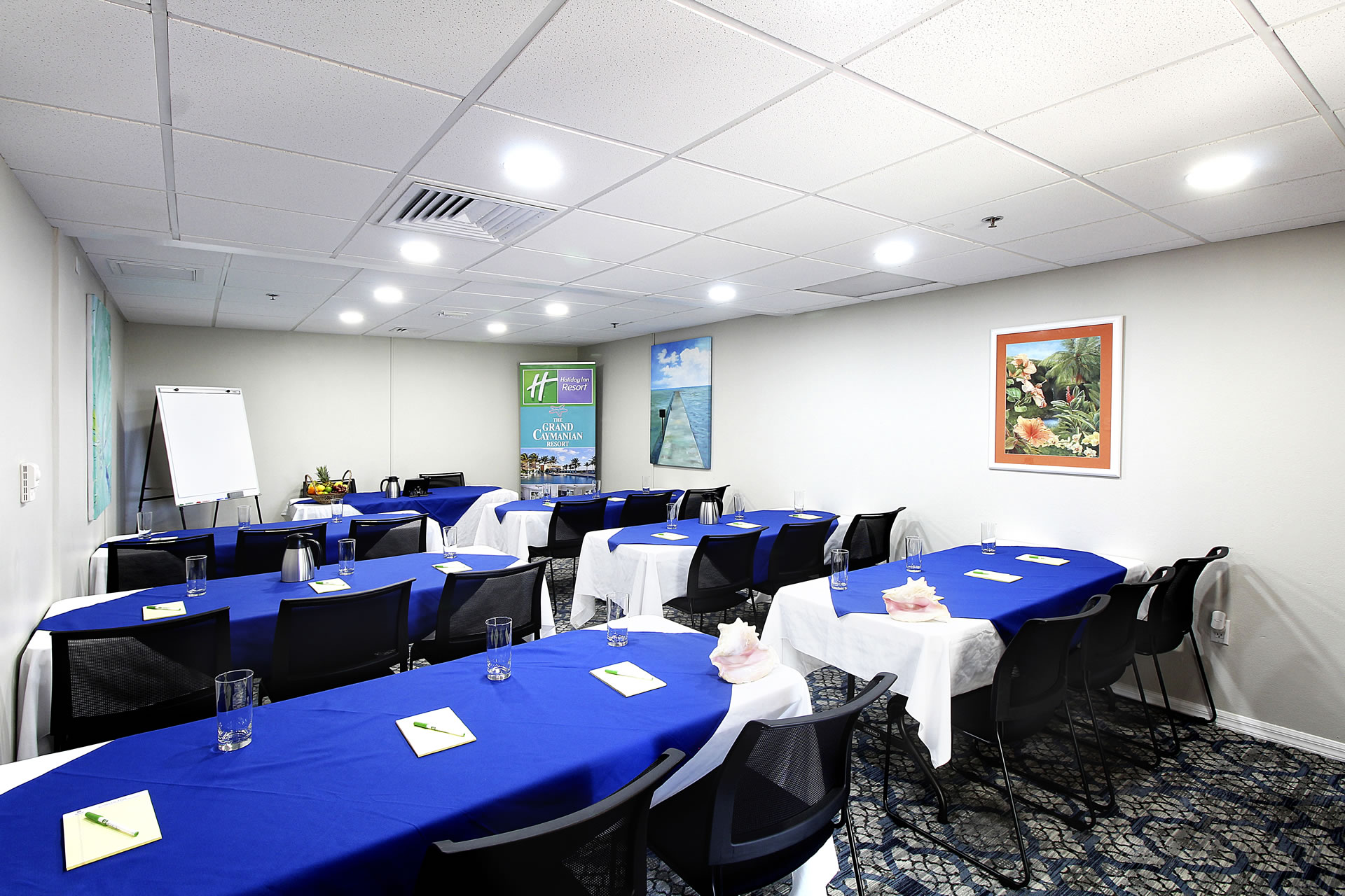 Meeting space at the Grand Caymanian Resort configured in a classroom layout with blue and white table coverings and table, banner, and easel at the front of the room.
