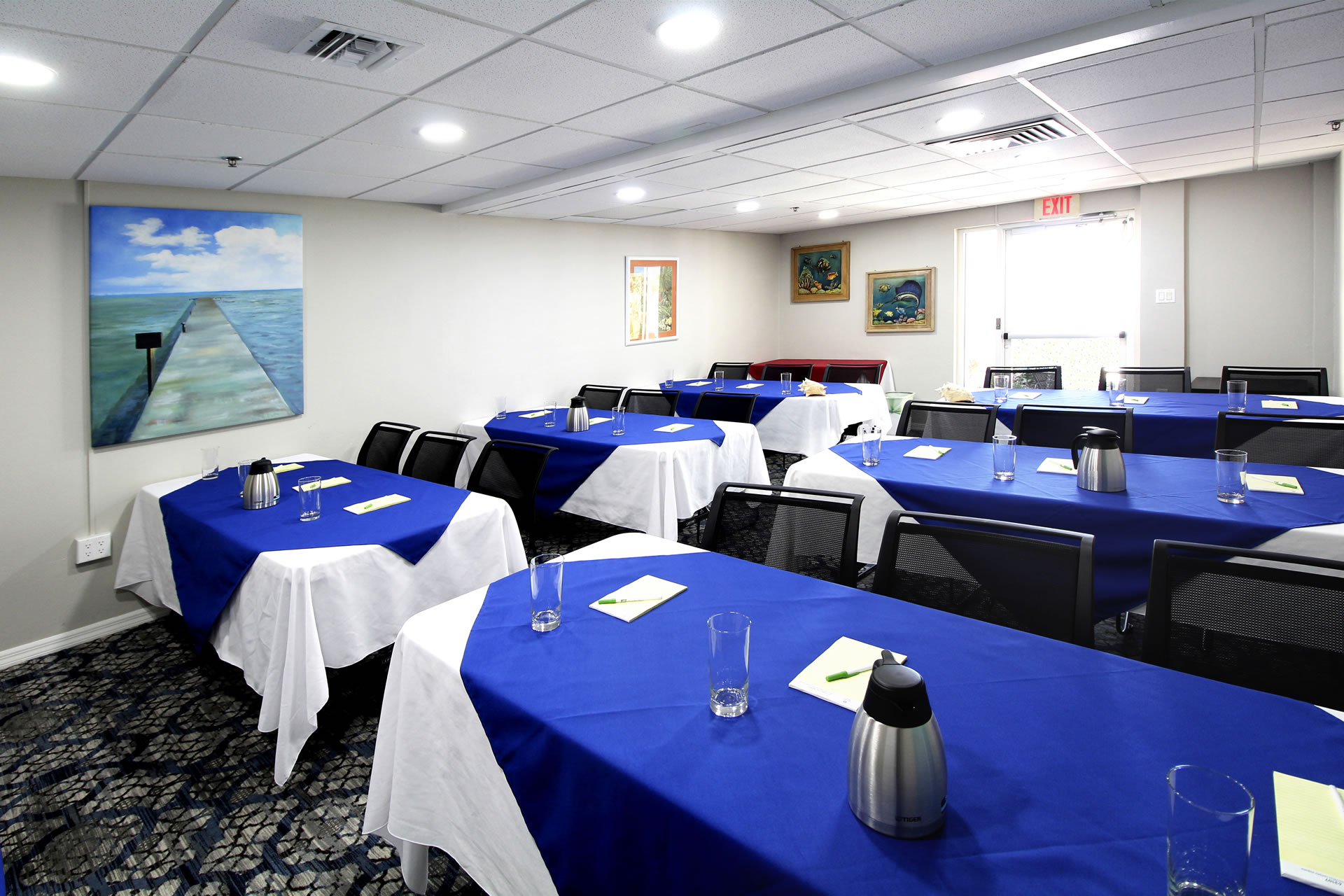 Meeting space at the Grand Caymanian Resort configured in a classroom layout with blue and white table coverings and an exit door at the back of the room.
