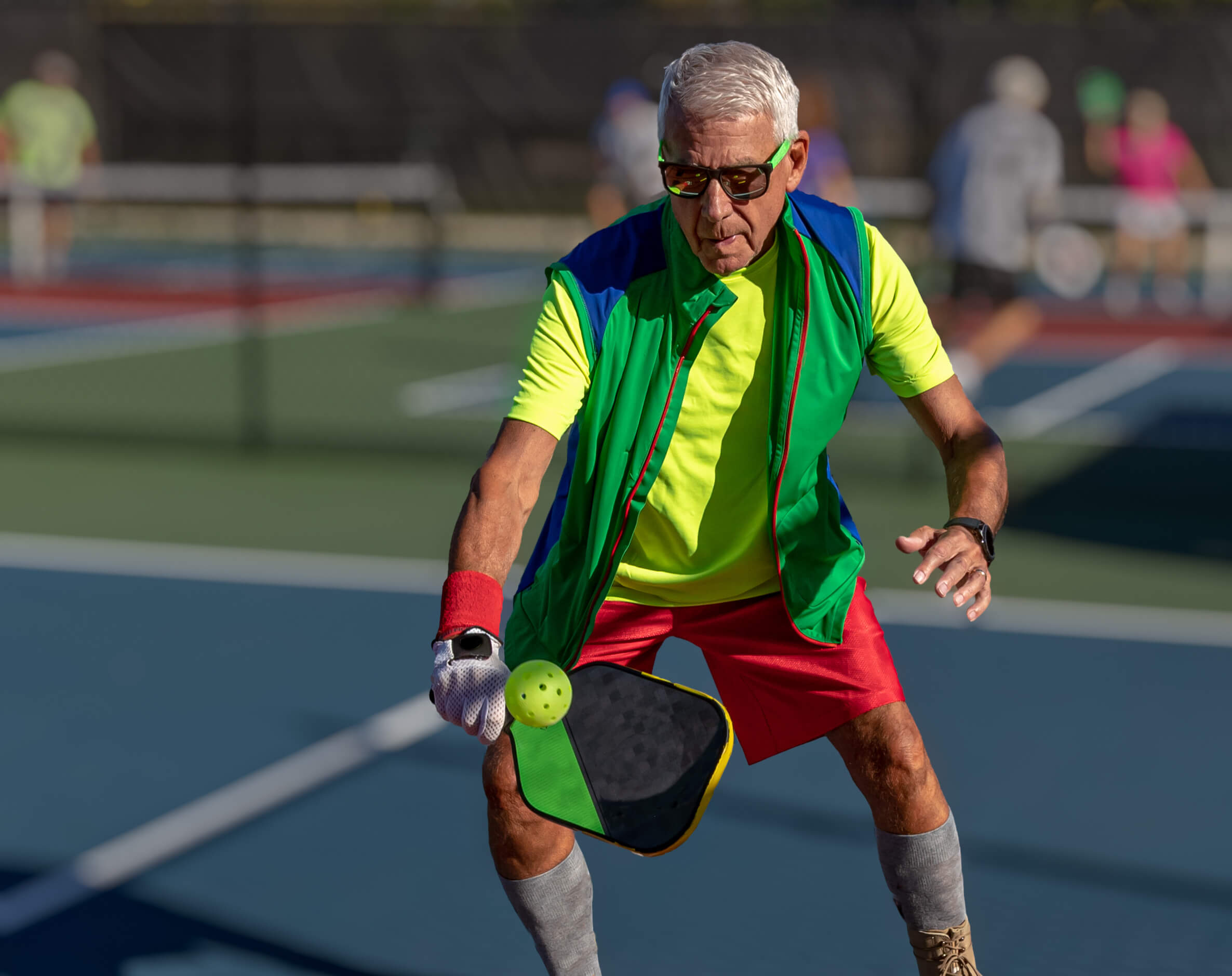 Older man in sunglasses playing pickleball.