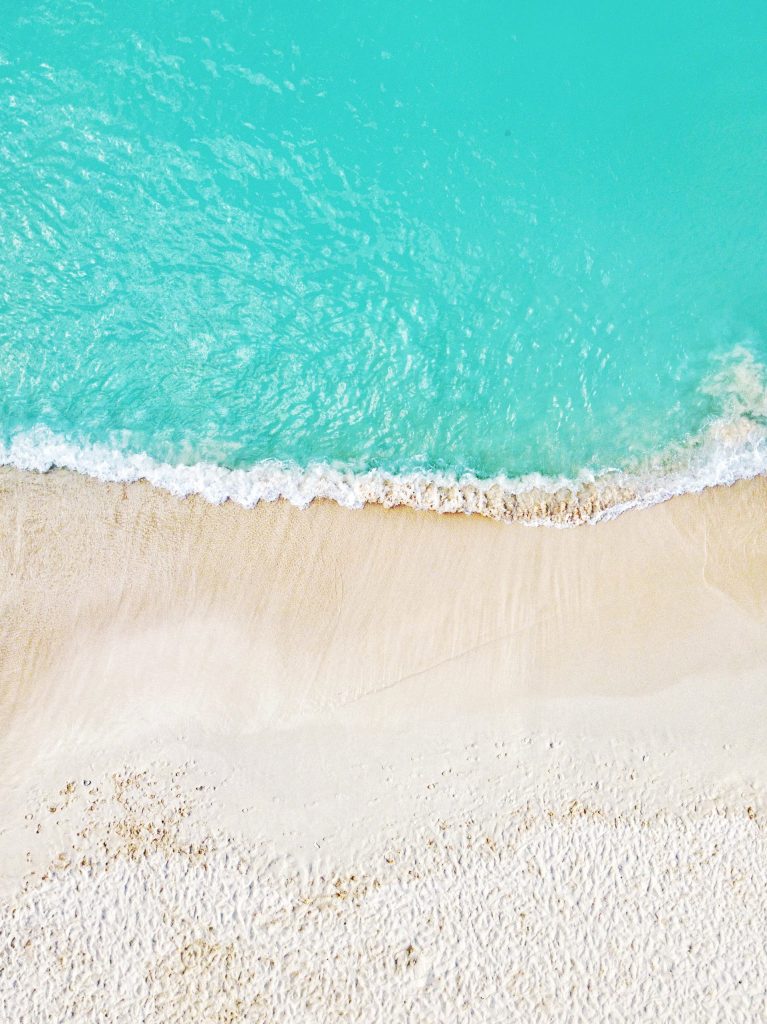 Birds-eye view of turquoise ocean waves lapping at a white sandy beach.