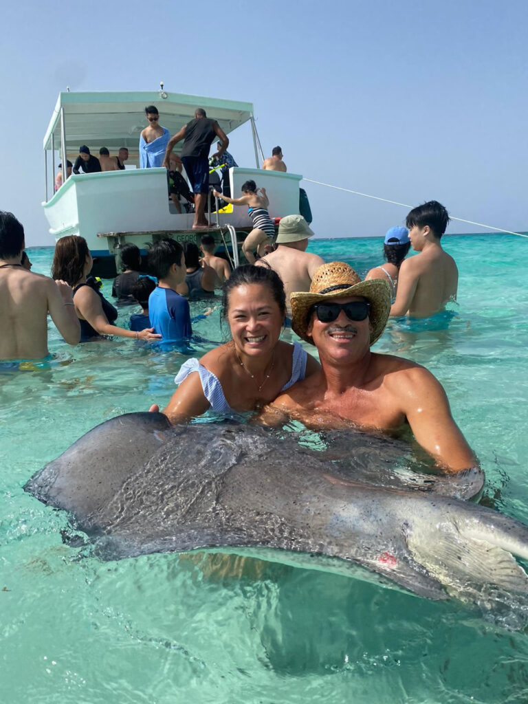 Man and woman in the ocean with stingray during a Cayman Sun Splash Tour.