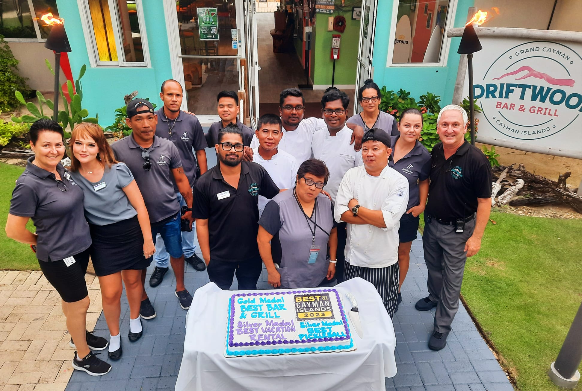 Staff at Driftwood Bar & Grill at The Grand Caymanian Resort posing near a cake celebrating their restaurant's recent Best of Grand Cayman 2023 gold award.