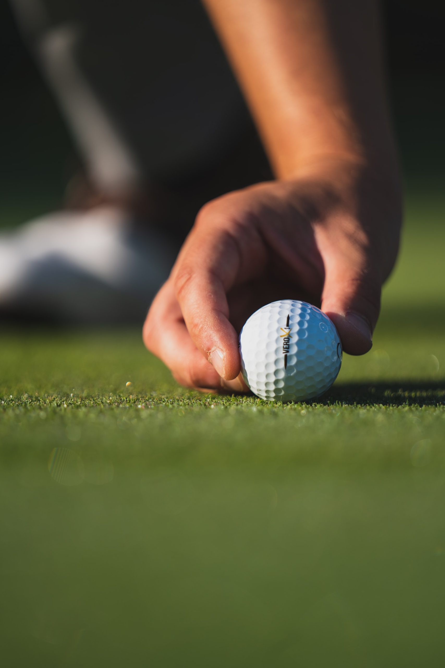 A close up of a hand setting a golf ball on the green.