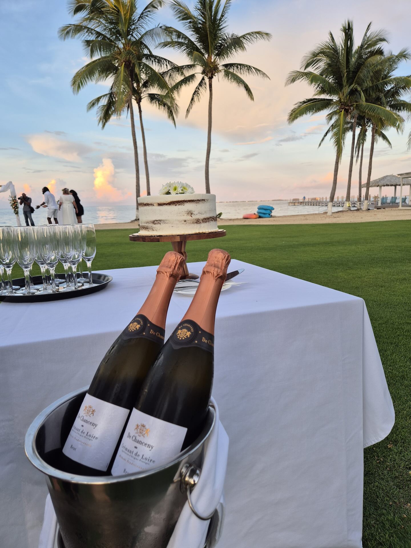 Bottles of champagne next to a wedding cake on a table with the beach in the background.