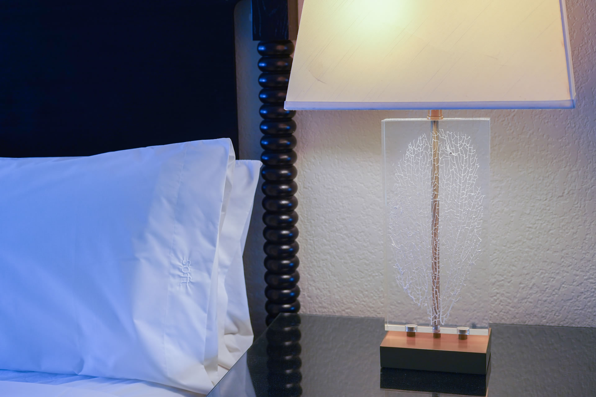 Close up of bed pillow and coral decor within the nightstand lamp in the One Bedroom King Suite at the Grand Caymanian Resort.