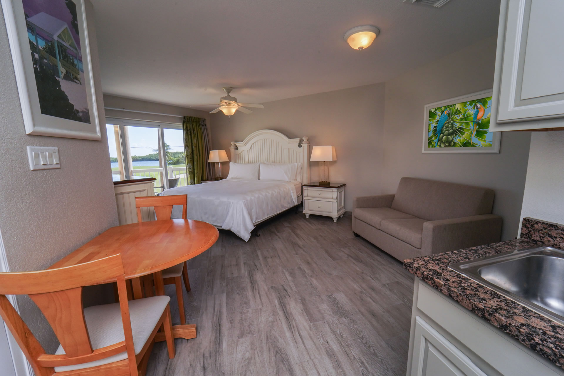 Queen bed, sleeper sofa, dining table, kitchen sink, and sunny balcony facing the golf course in the One Queen Bed Studio Suite with Sleeper Sofa at the Grand Caymanian Resort.