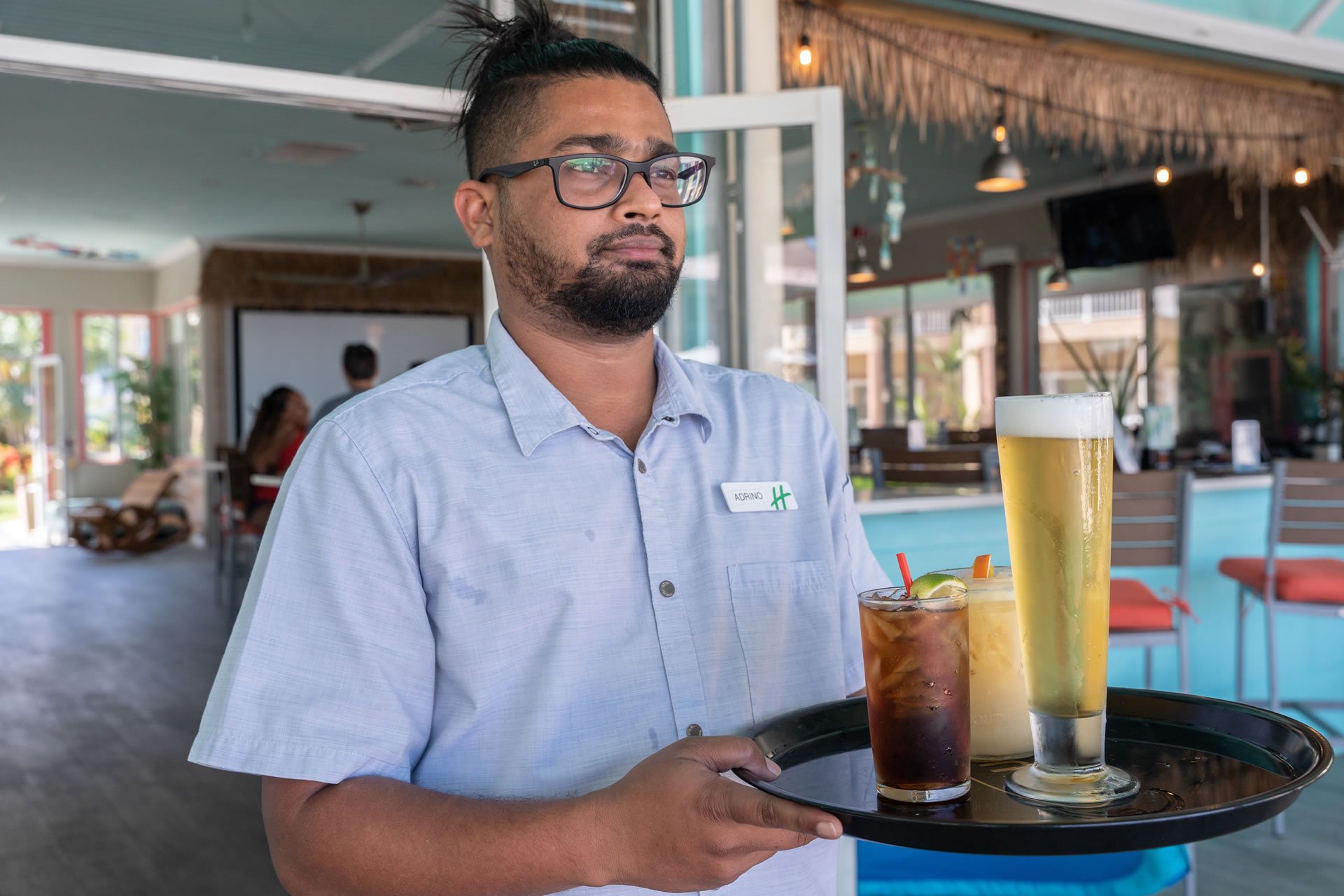 A server carrying a platter of beverages at the Driftwood Bar and Grill within the Grand Caymanian Resort.