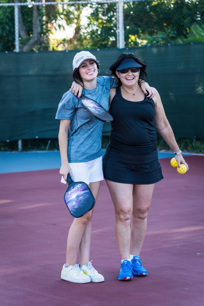 Young woman with her arm around an older woman on a pickelball court at the Grand Caymanian Resort.