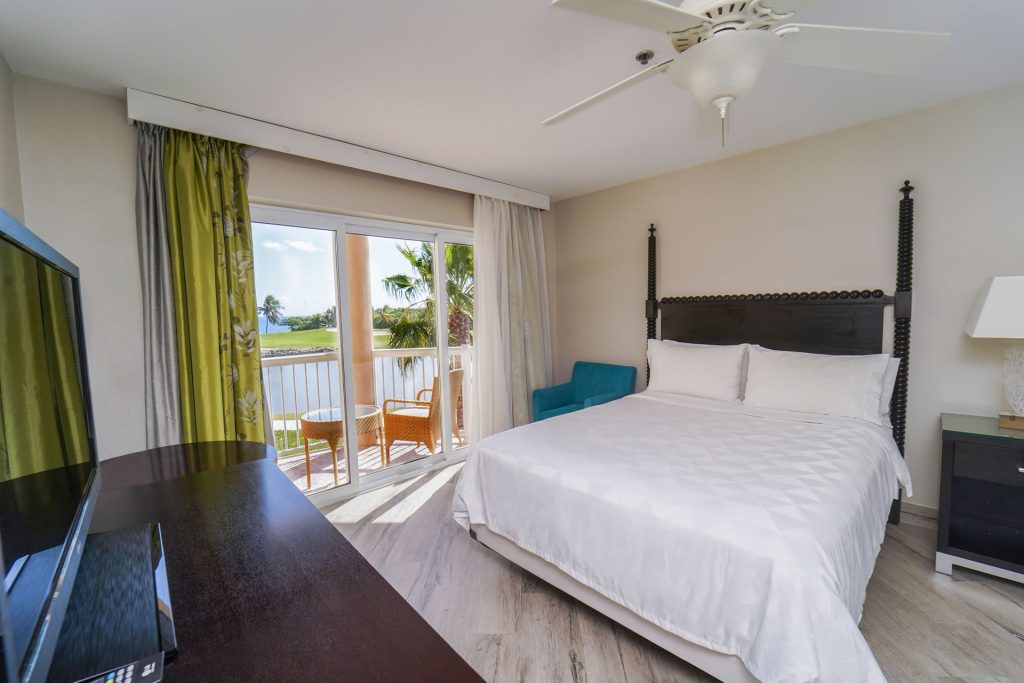 Queen bed and sunny balcony facing the North Sound Golf Club in the One Queen Bed Studio Suite with Sleeper Sofa at the Grand Caymanian Resort.