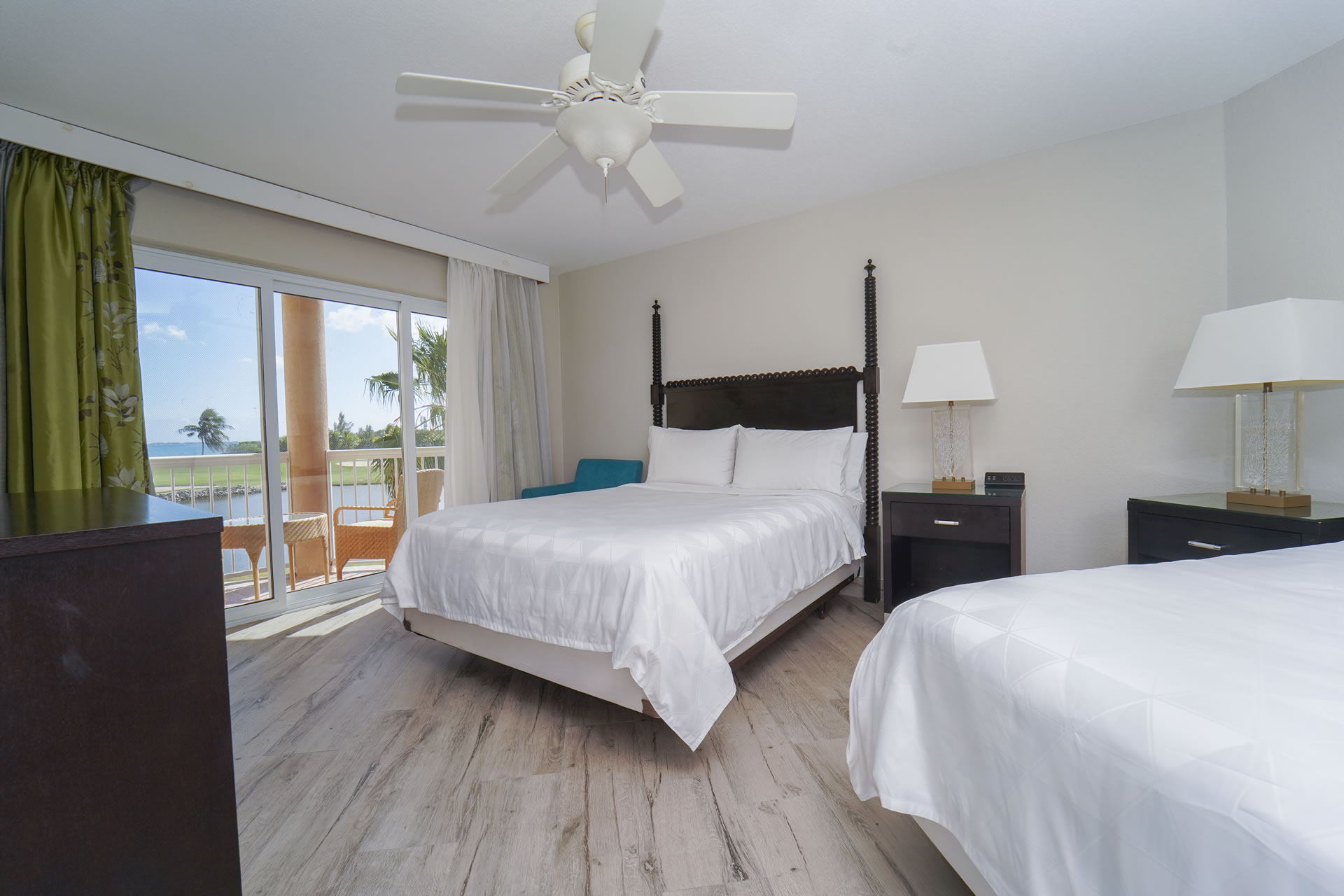 Two queen beds next to a sunny balcony facing the golf course in the Two Queen Bed Studio Suite at the Grand Caymanian Resort.