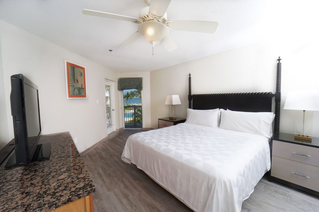 King bed, night stand, and balcony with ocean views in the One Bedroom King Suite at the Grand Caymanian Resort.