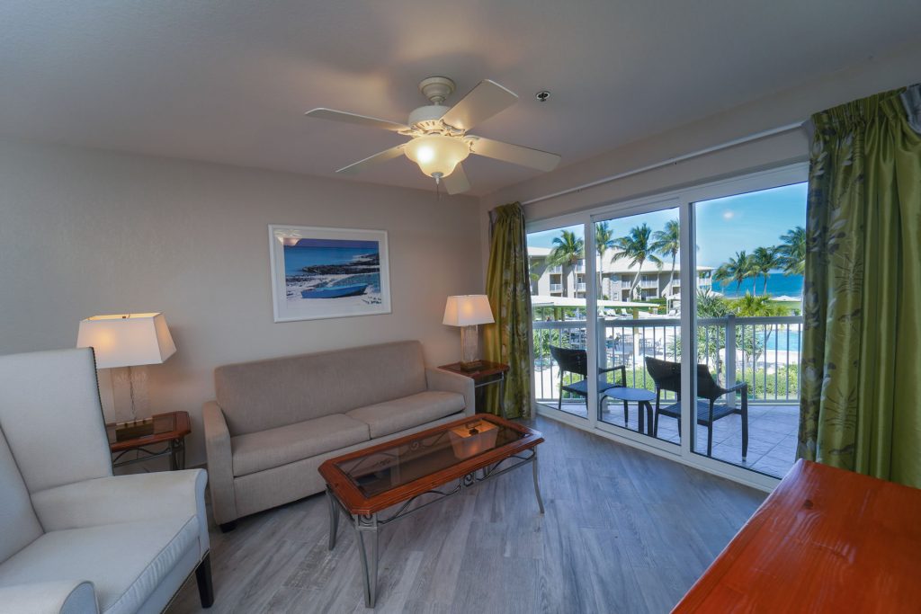 Living room and sunny balcony with ocean views in the One Bedroom King Suite at the Grand Caymanian Resort.