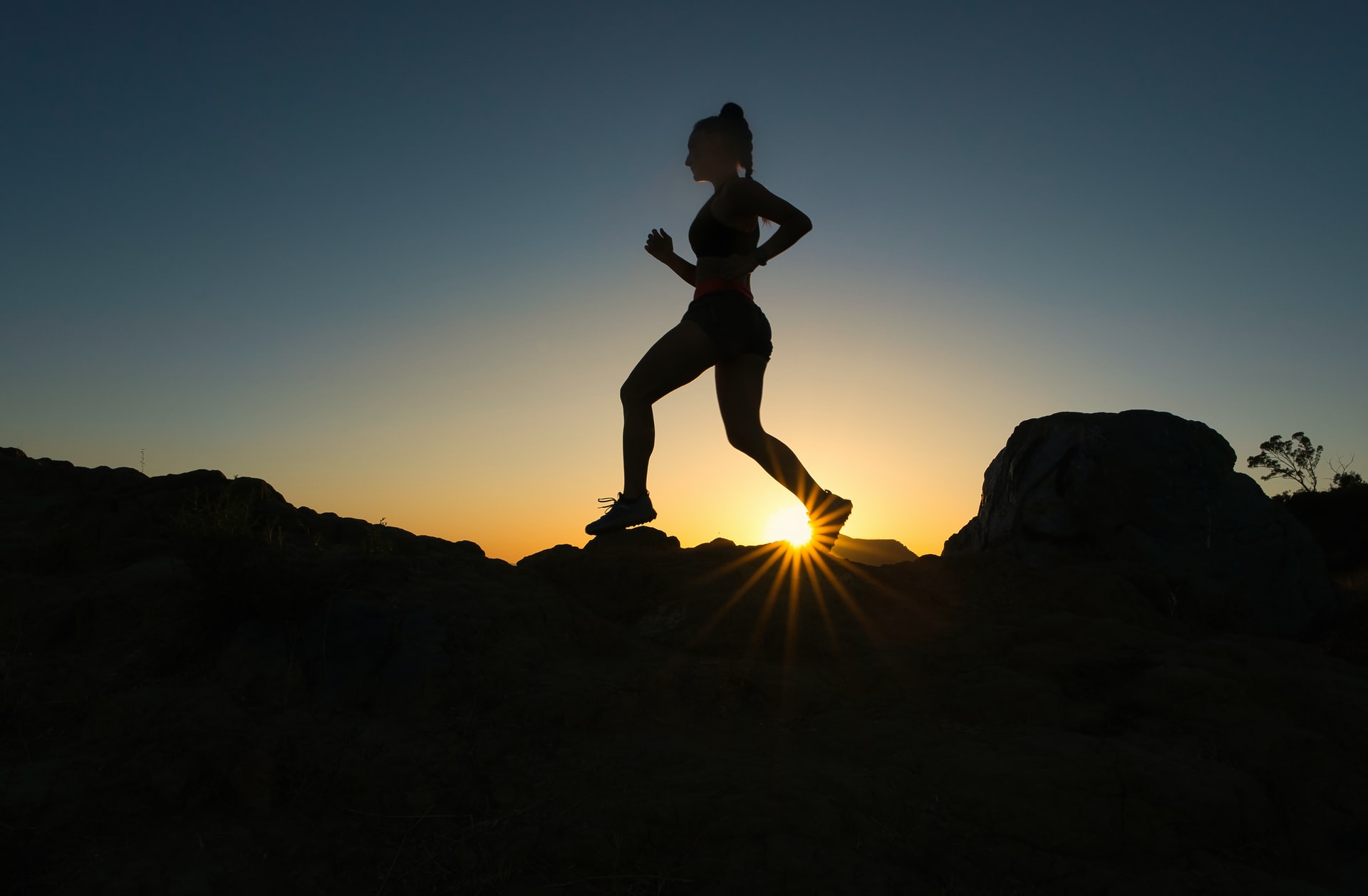 Silhouette of a woman running along a trail with the sunrise in the background.