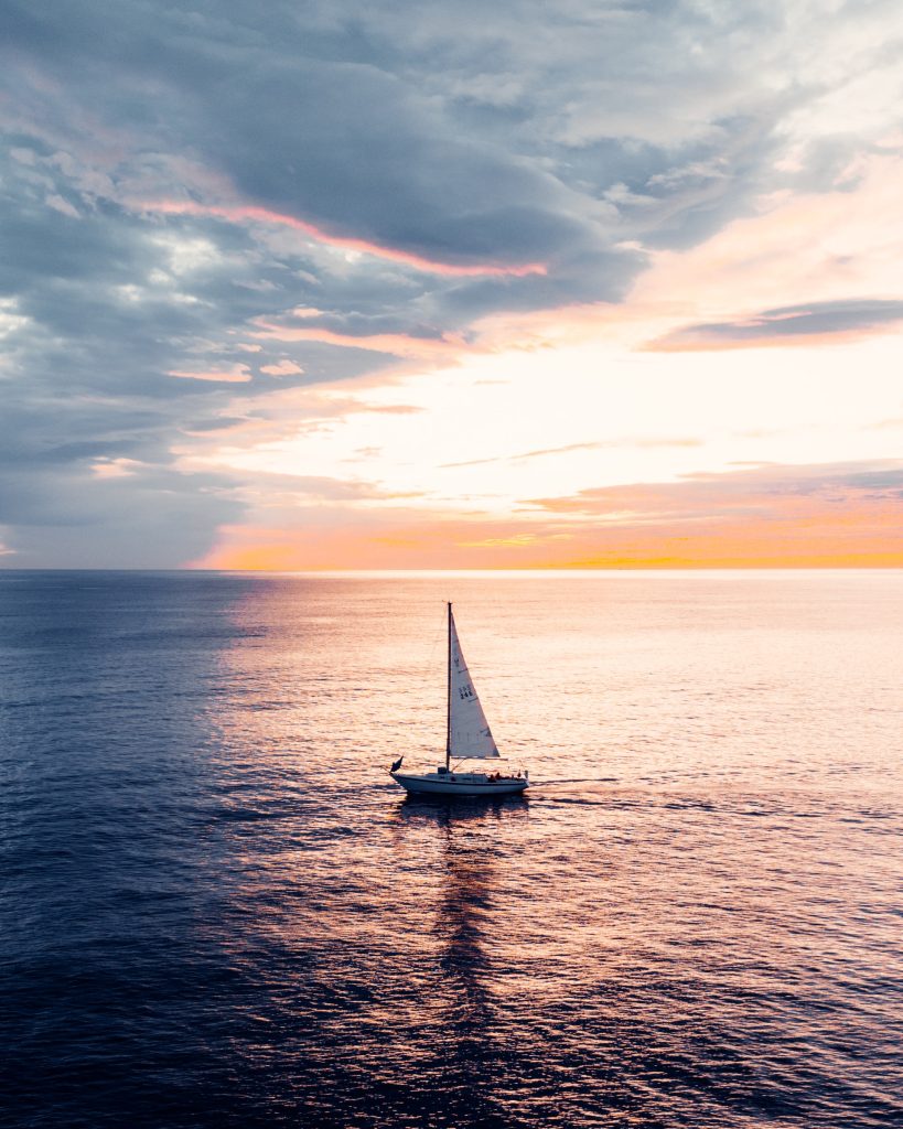 A sailboat alone on the ocean at sunset.